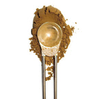 A metal scoop filled with a light tan powder, set against a background of spilled matching powder on a white studio background.